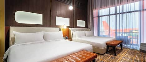 A hotel room with two beds, a bench, a nightstand, and a large window with a view.