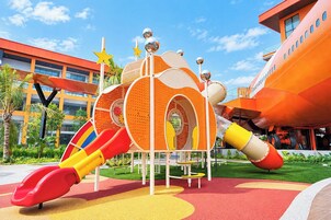 Un parque infantil con estructuras de juego coloridas, incluyendo un tobogán con forma de cohete y una cúpula con estrellas.