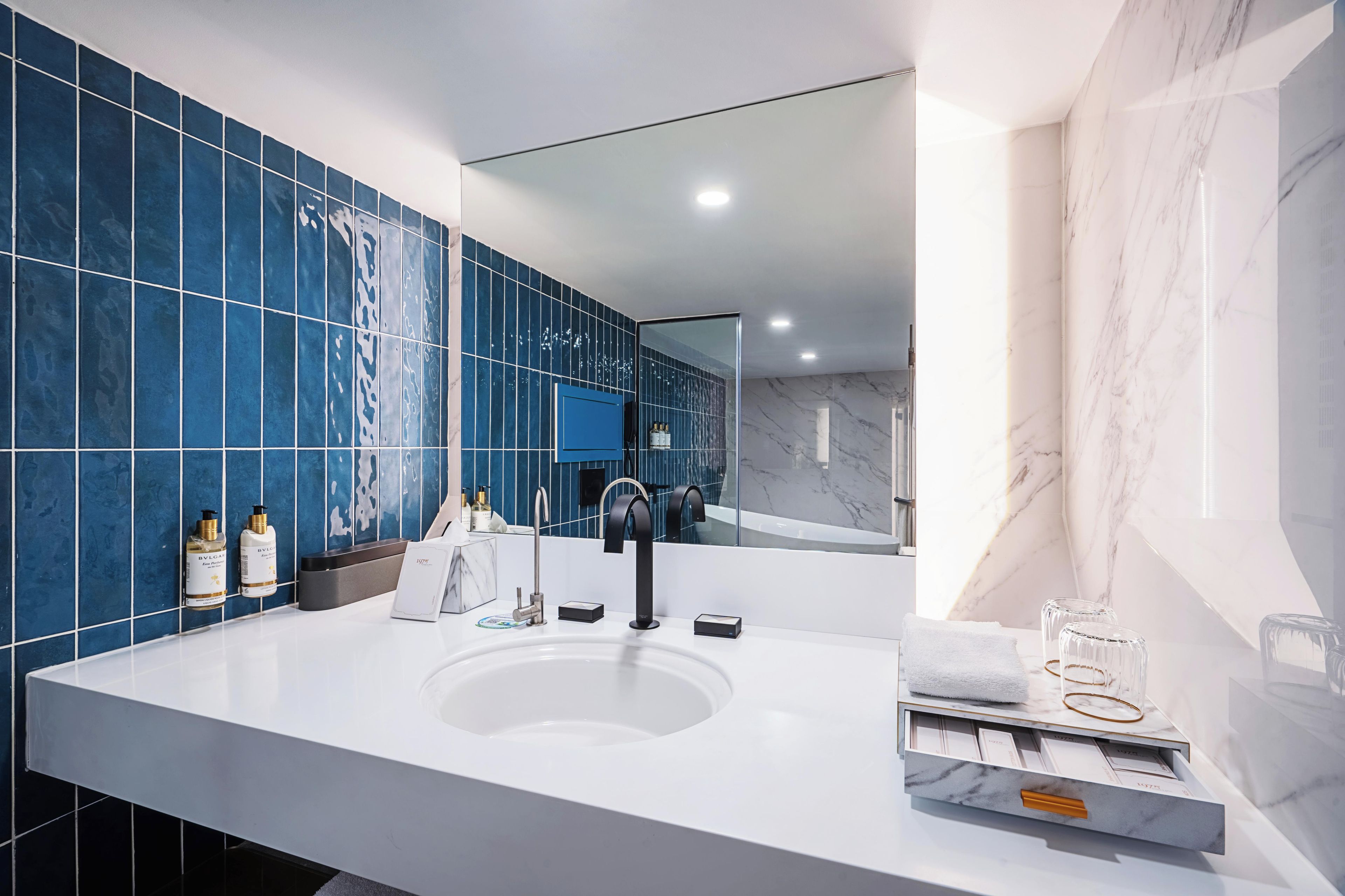 A modern bathroom with a large mirror, a white sink, and blue tiles on the walls.
