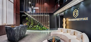 Un hall d’entrée moderne avec un comptoir de réception en pierre, un canapé blanc, un escalier orné de fauteuils suspendus et un mur sur lequel figure un logo et du texte.
