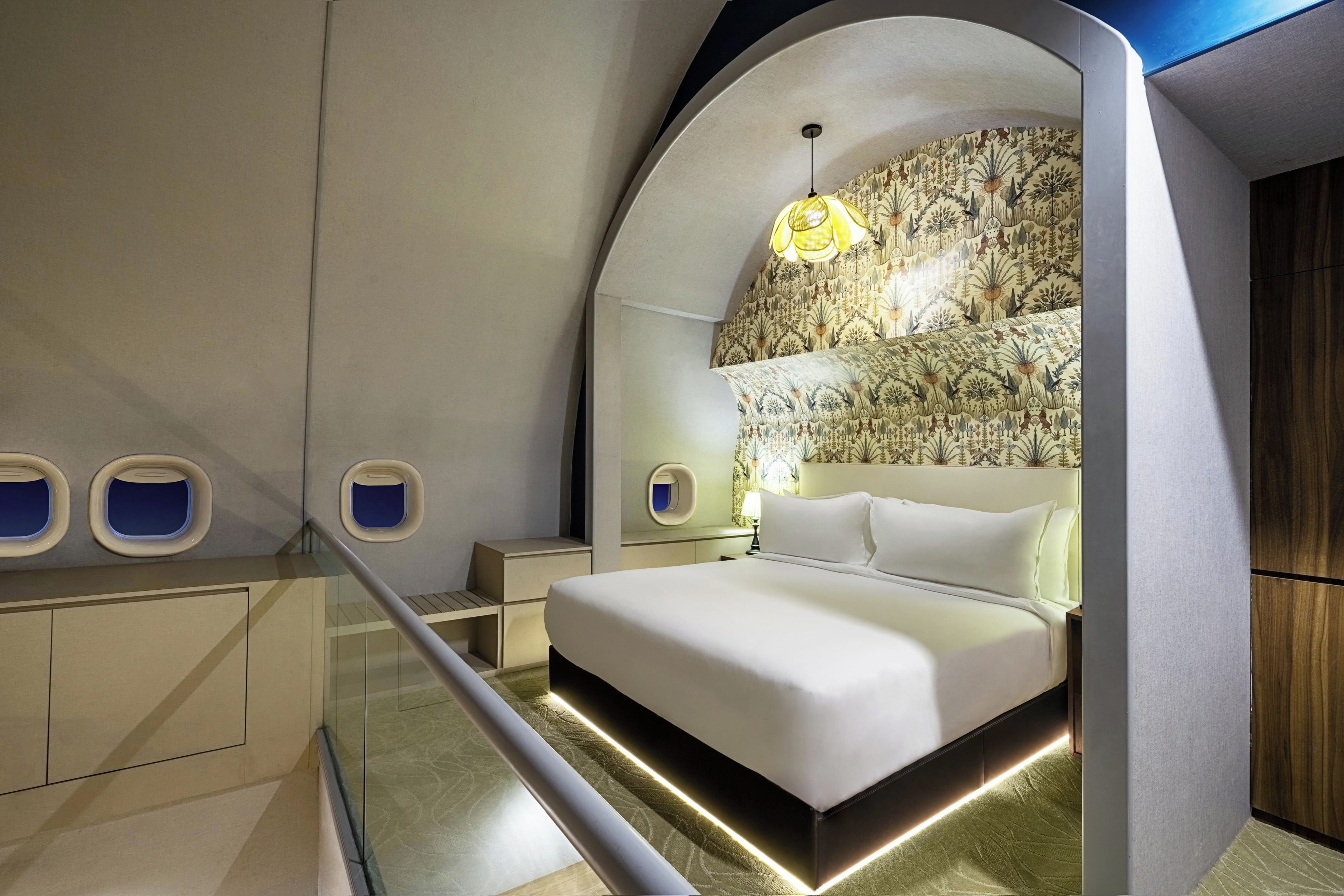 A modern bedroom with a large bed, a nightstand, a lamp, and a unique wall design.