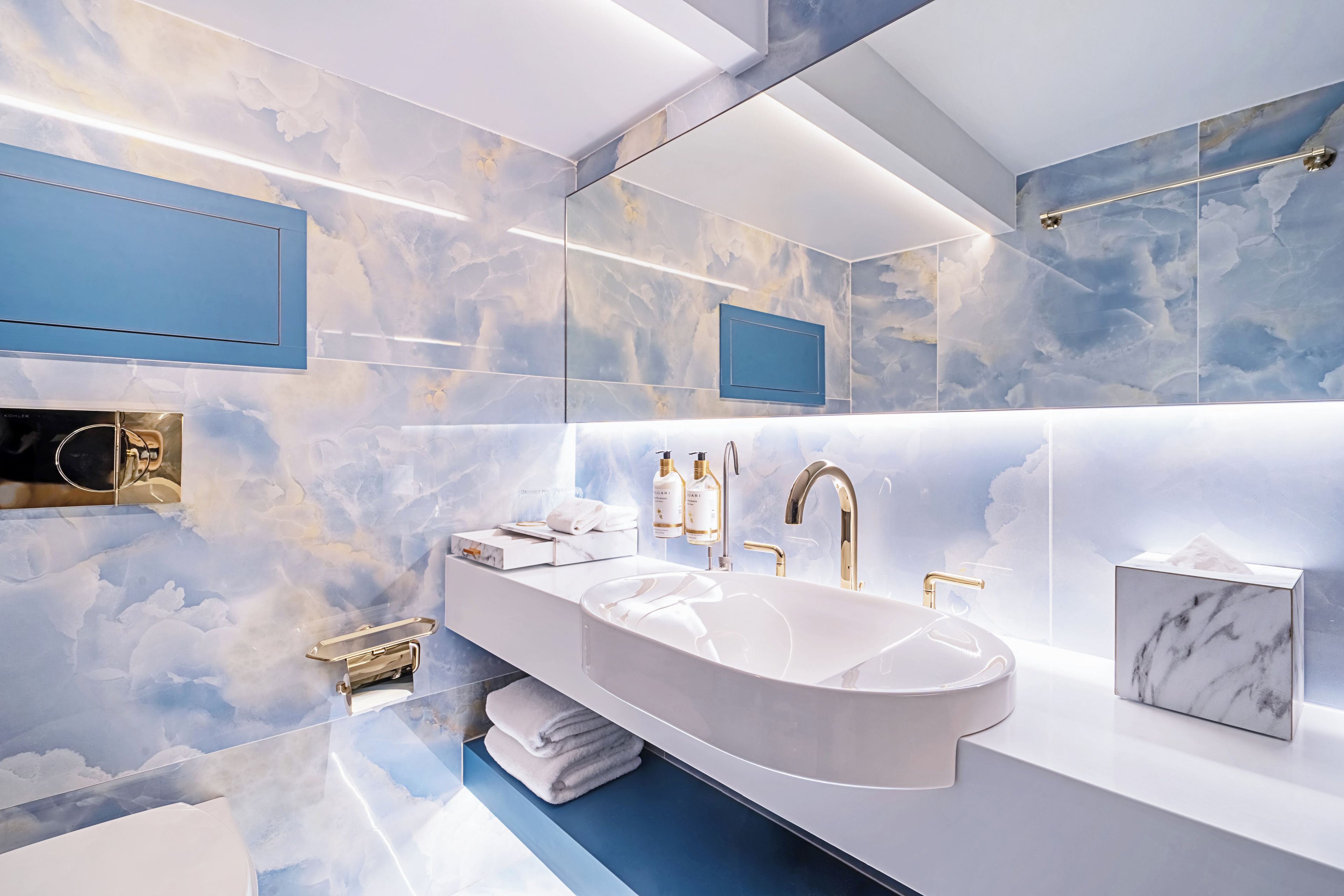 A modern bathroom with a large marble sink, gold fixtures, and a cloud-themed wall design.