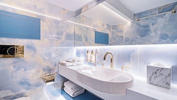 A modern bathroom with a large marble sink, gold fixtures, and a cloud-themed wall design.