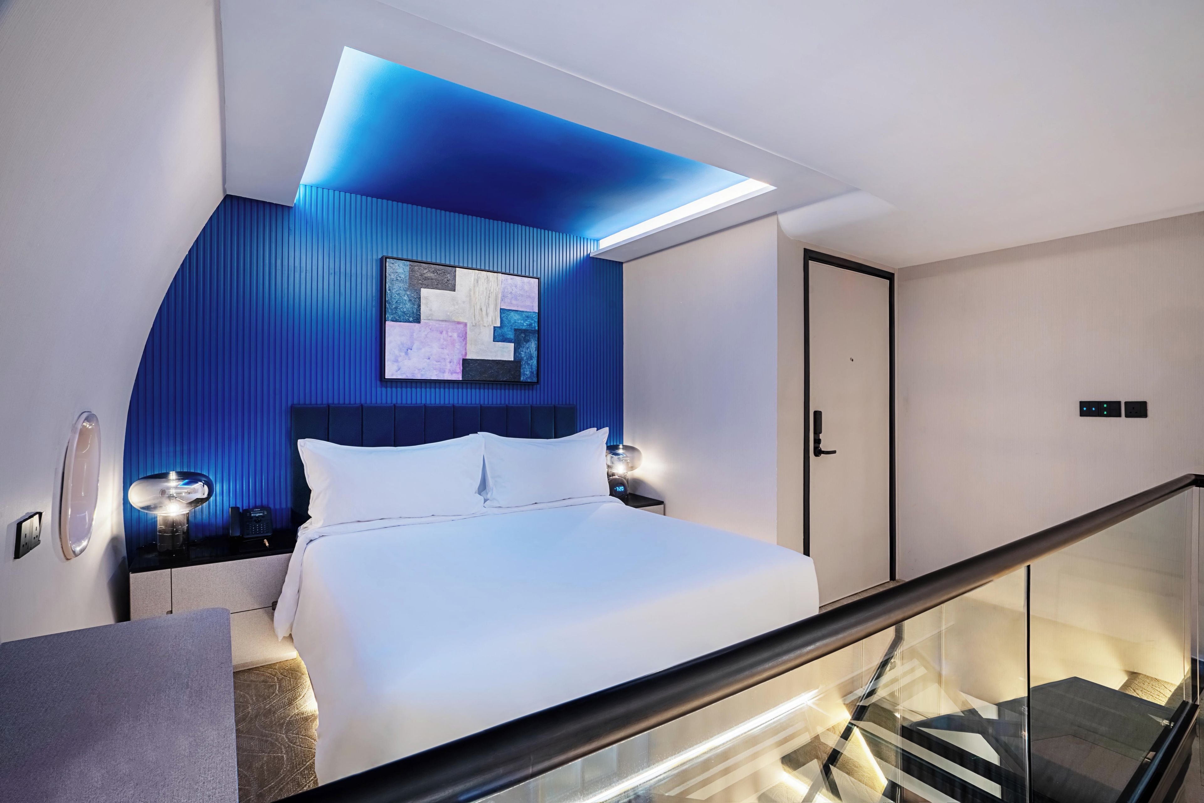 A modern bedroom with a bed, bedside tables, a nightstand, a wall-mounted artwork, and a door.