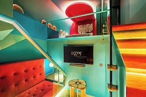 Una escalera con una zona de estar acolchada de color rojo, un cartel en la pared que indica '1975 Avenue & Hotel by Tiong Nam', y un adorno de macramé.