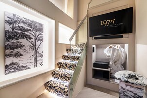 A staircase with patterned carpet, a framed black and white tree painting, a black sign with '1975 Avenue & Road by Tiong Nam', and a robe hanging on a hook.