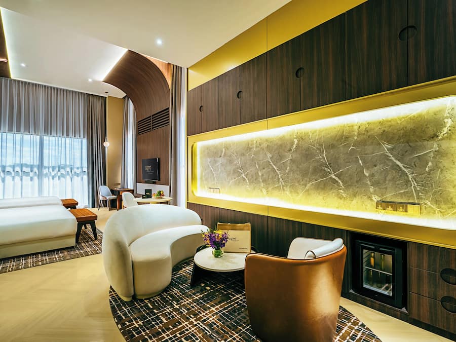 A modern hotel room with a large bed, a curved sofa, a small round table, and a unique wall-mounted light fixture.