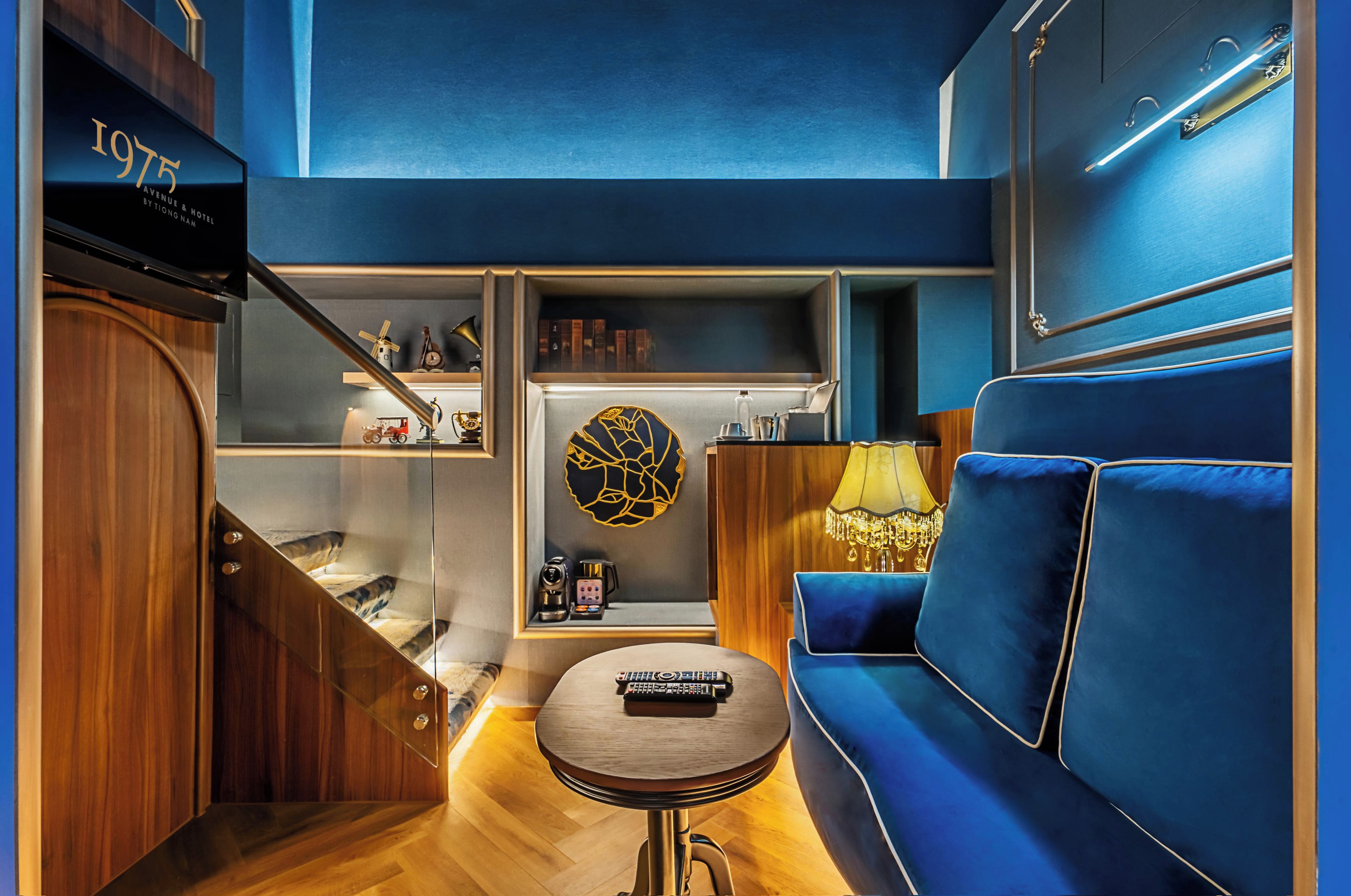 A modern hotel room with a blue sofa, a small round table, and a bookshelf with decorative items.