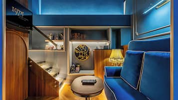 A modern hotel room with a blue sofa, a small round table, and a bookshelf with decorative items.