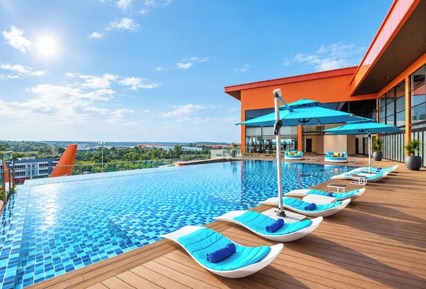 Un espace piscine moderne, doté de chaises longues et de parasols, entouré d’une terrasse en bois et offrant une vue sur le paysage urbain.