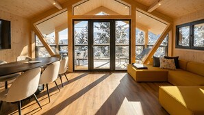 En modern inredning med ett träpanelat tak, en matplats med stolar, en soffa och en stor skjutdörr i glas som leder ut till ett snötäckt utomhusområde.