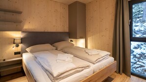 Ett sovrum i en stuga med träpanel, en säng, sänglampor och ett fönster med gardiner.