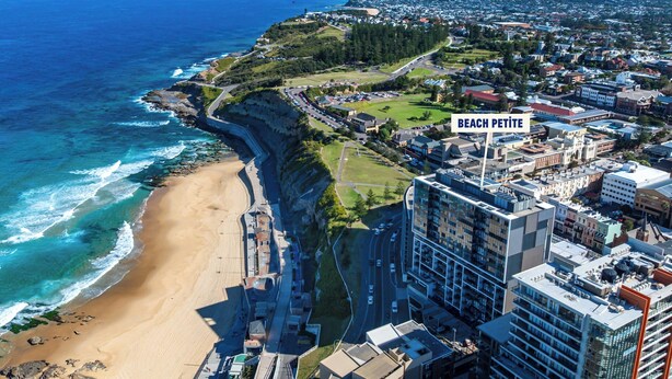 An aerial view of Beach Petite with a beach, buildings, and a road. - Beach Petite - Across from Beach - Walk to City (Newcastle)