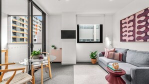 A modern living room with a sofa, a glass table, and a red side table. - Beach Petite - Across from Beach - Walk to City (Newcastle)