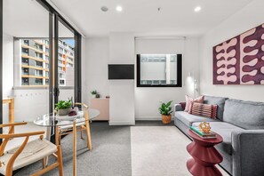 Uma sala de estar moderna com um sofá, uma mesa de vidro e uma mesinha lateral vermelha.