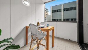 A balcony with a wooden table, two chairs, a bottle, and a glass. - Beach Petite - Across from Beach - Walk to City (Newcastle)