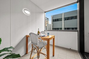 A balcony with a wooden table, two chairs, a bottle, and a glass. - Beach Petite - Across from Beach - Walk to City (Newcastle)