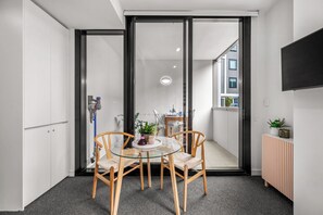 A modern room with a glass table, wooden chairs, a small plant, and a TV on the wall. - Beach Petite - Across from Beach - Walk to City (Newcastle)