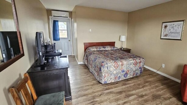 A hotel room with a bed, a desk with a computer, a chair, a red armchair, and a wall-mounted TV. - Countryview Motel and Restaurant  (Steeves Mountain)