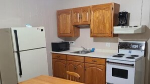 A compact kitchen with wooden cabinets, a refrigerator, a microwave, a stove, and a dining table with chairs. - Countryview Motel and Restaurant  (Steeves Mountain)