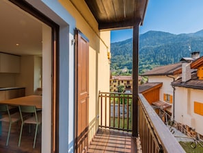 A balcony with a view of a mountain landscape, a dining area with a table and chairs, and a wooden door. - Ca' Alma Dolomia by Interhome (Strembo)