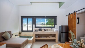 Ein kompakter Wohnbereich mit einer Küchenzeile, einem Sofa, einem Esstisch und Blick auf Grünflächen durch große Fenster.
