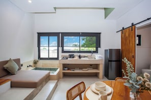 Espaço compacto para viver, com cozinha americana, sofá, mesa de jantar e vista para o verde através de amplas janelas.
