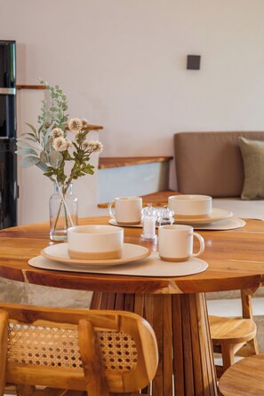 A wooden dining table with white plates, cups, and a vase with flowers. - Shanti - 1BR Loft1 in Uluwatu (Badung)