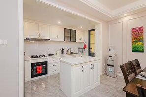 A modern kitchen with white cabinets, a built-in oven, a water dispenser, and a dining area with a table and chairs. - Upscale 3-Bedroom Apartment in Prime Kilimani (Nairobi)
