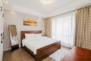 Ett modernt hotellrum med en säng i trä, ett stort fönster med tunna, genomskinliga gardiner, en tavla på väggen och en spegel med en träram.