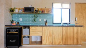 A compact kitchen with a blue-tiled backsplash, wooden cabinets, a built-in microwave, and a Marshall amplifier. - Boho 1-Bedroom Apartment with Fast Wi-Fi in Downtown, Perfect for Working Near the Hotel District (Cancún)