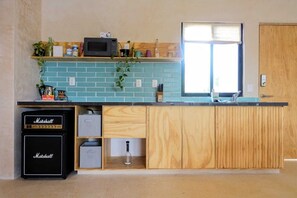 A compact kitchen with a blue-tiled backsplash, wooden cabinets, a built-in microwave, and a Marshall amplifier. - Boho 1-Bedroom Apartment with Fast Wi-Fi in Downtown, Perfect for Working Near the Hotel District (Cancún)