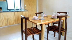 A dining area with a wooden table and chairs, a kitchen in the background, and a window with blinds. - Boho 1-Bedroom Apartment with Fast Wi-Fi in Downtown, Perfect for Working Near the Hotel District (Cancún)