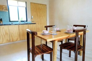 A dining area with a wooden table and chairs, a kitchen in the background, and a window with blinds. - Boho 1-Bedroom Apartment with Fast Wi-Fi in Downtown, Perfect for Working Near the Hotel District (Cancún)
