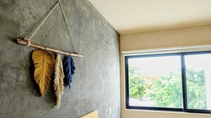A room with a concrete wall, a wooden bed, and a window with a view of greenery. - Boho 1-Bedroom Apartment with Fast Wi-Fi in Downtown, Perfect for Working Near the Hotel District (Cancún)