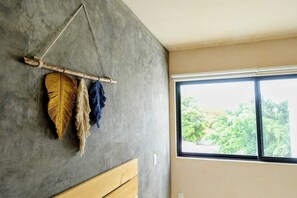 A room with a concrete wall, a wooden bed, and a window with a view of greenery. - Boho 1-Bedroom Apartment with Fast Wi-Fi in Downtown, Perfect for Working Near the Hotel District (Cancún)