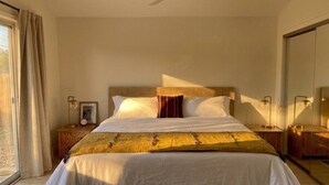 Ein Hotelzimmer mit einem Bett, einem Deckenventilator, einem Nachttisch mit Lampe, einem Spiegel und einem fenster mit Vorhängen.