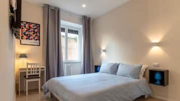 Ein Schlafzimmer mit Bett, Stuhl, Schreibtisch, Fenster und einer Wandleuchte.