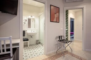 Ein Hotelzimmer mit weißem Stuhl, einem kleinen Tisch, einem Badezimmer mit Waschbecken und Spiegel sowie einem gestreiften Boden.