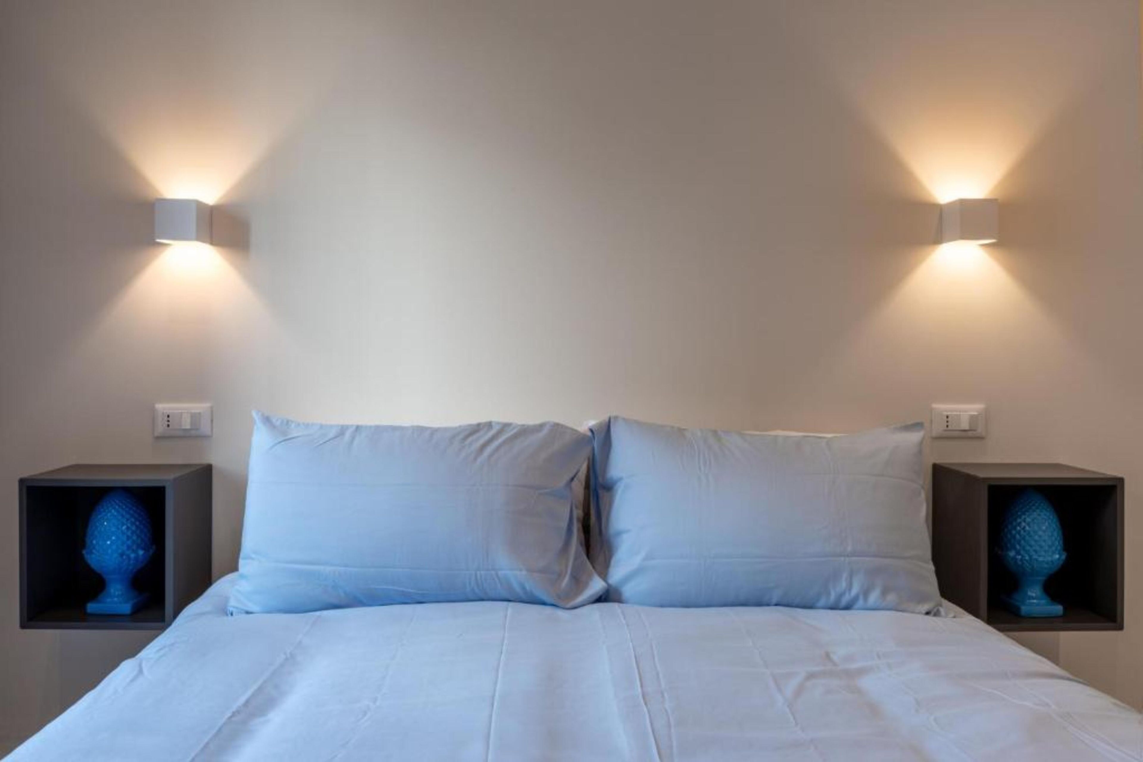A bed with white bedding and two nightstands with blue decorative objects.