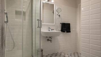 Un baño con cabina de ducha de vidrio, un lavabo blanco y un espejo.