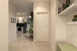 A modern kitchen with white cabinets, a dining area with a green chair, and a white door leading to another room. - Brick & Arch (Roma)