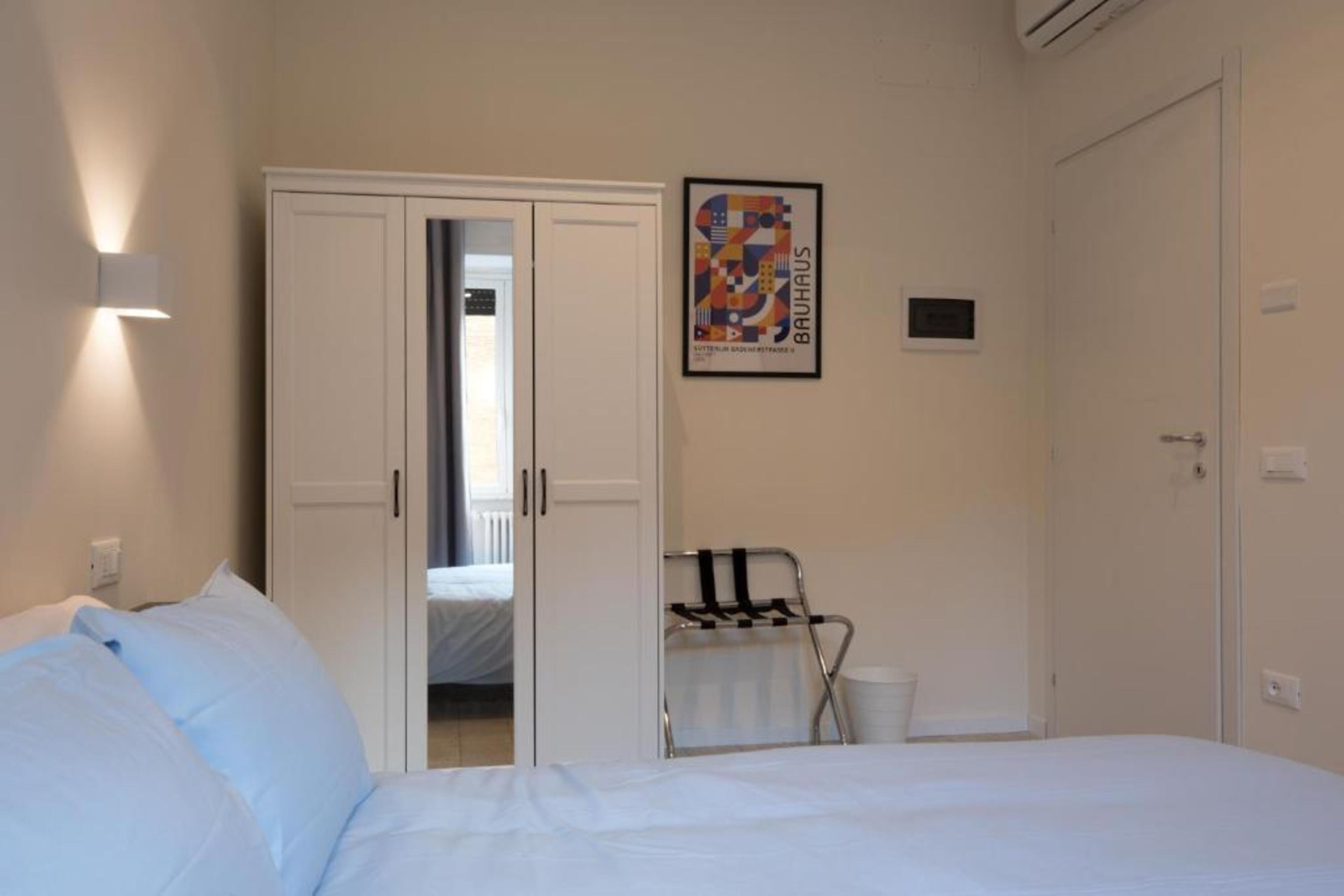 A hotel room with a bed, a wardrobe, a radiator, and a poster on the wall.
