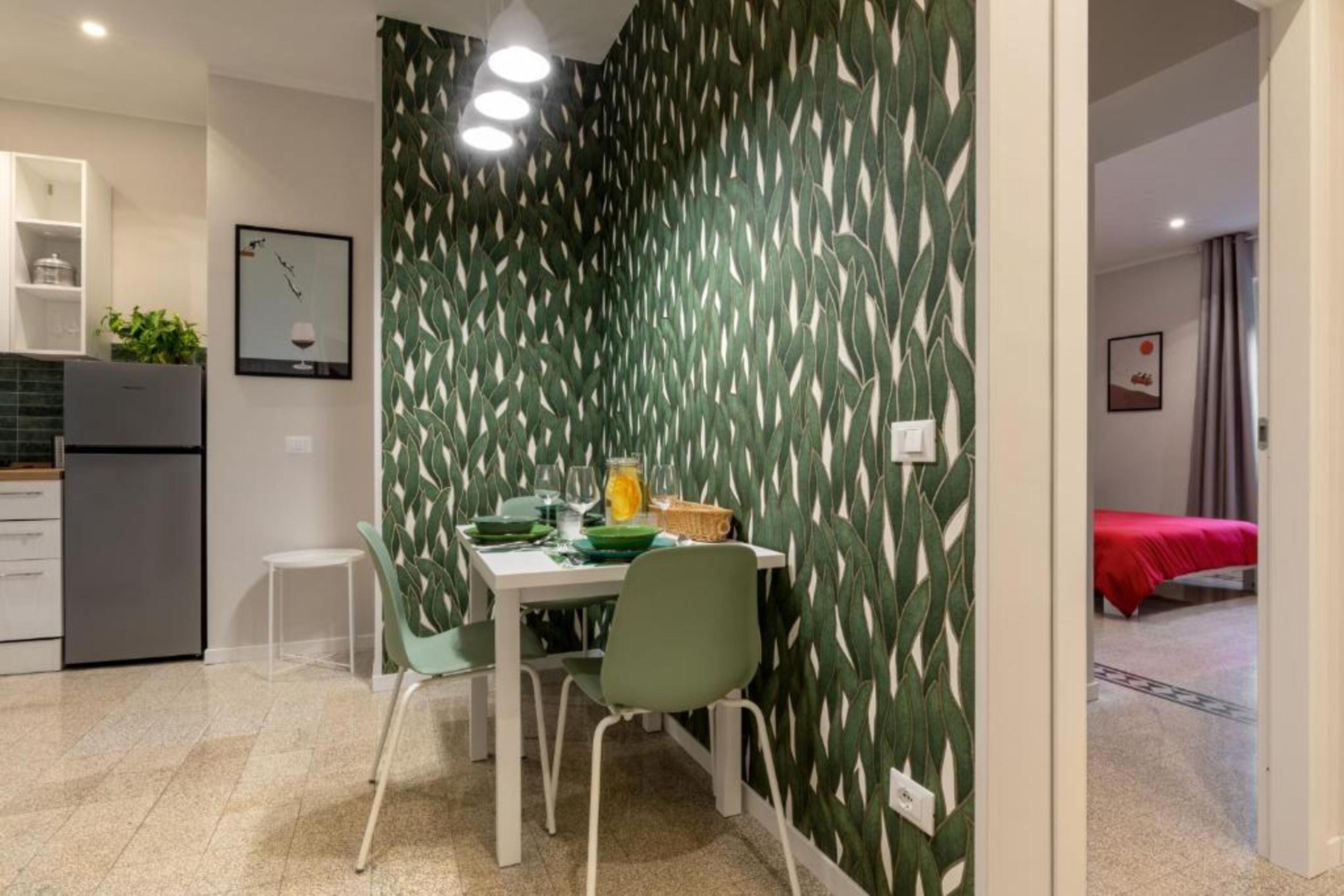 A compact kitchen with modern appliances, a dining area with a table and chairs, and a bedroom with a red bedspread.