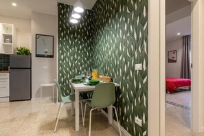 Una cocina compacta con electrodomésticos modernos, un comedor con mesa y sillas, y un dormitorio con colcha roja.