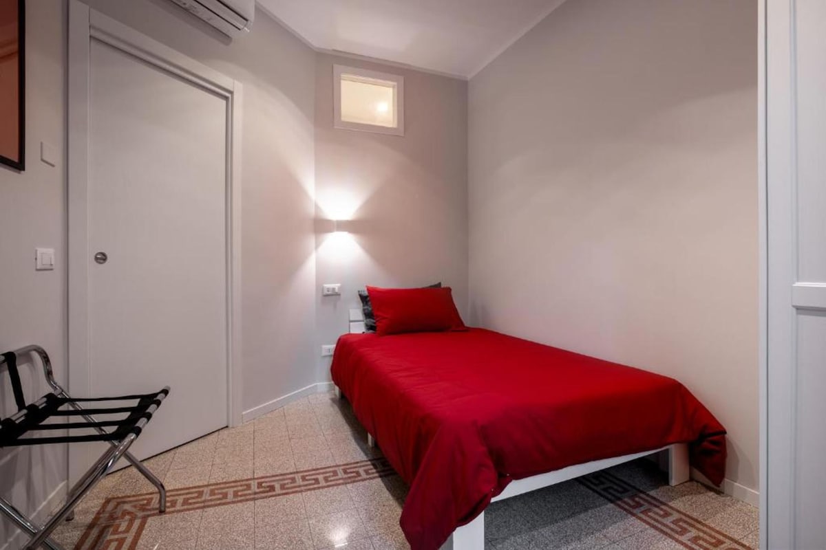 A small, well-lit bedroom with a single bed, a chair, and a small window.