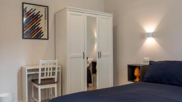 A bedroom with a bed, a wardrobe, a desk with a chair, and a wall-mounted light fixture.
