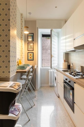 A compact kitchen with a dining area, a radiator, and a window. - Brick & Arch (Roma)