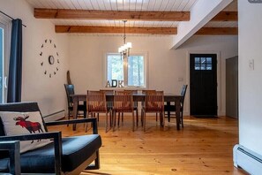 A dining area with wooden tables and chairs, a chandelier, and a wall clock. - The Black Pine at ADK 10 minutes to Whiteface (Jay)