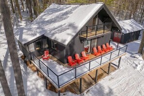 A cabin with a balcony and red chairs, surrounded by trees and snow.